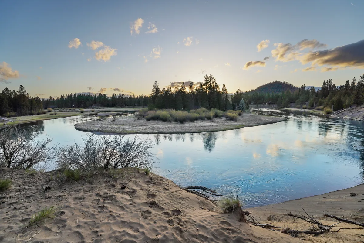 A serene view of a winding river bordered by lush trees and gentle hills, with the water beautifully reflecting the sky. The landscape invites outdoor exploration, wildlife watching, and tranquil walks along the riverbank—activities perfect for guests with pets.