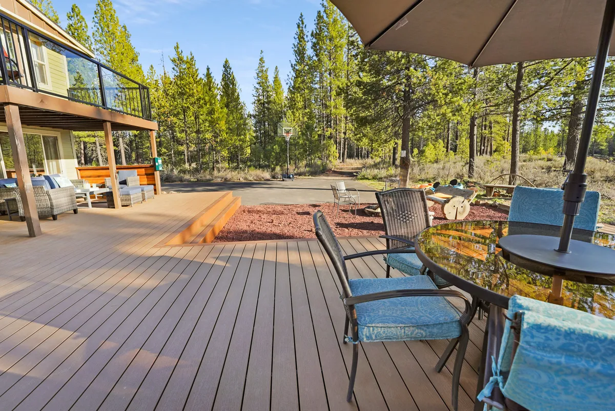 A spacious exterior deck with a dining table, comfortable seating, and a basketball hoop set against a backdrop of trees. The area is ideal for outdoor dining, relaxing, and group activities like basketball or board games, showcasing the perfect spot for families or groups to gather and enjoy each other's company surrounded by nature.