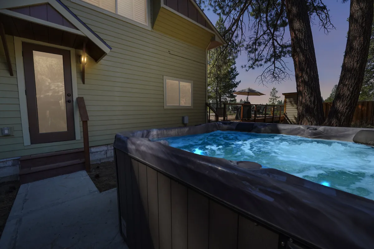 A private hot tub sits on a deck near the entrance, surrounded by trees for privacy and natural ambiance. The hot tub area looks serene and inviting, perfect for stargazing or unwinding after a day outdoors.