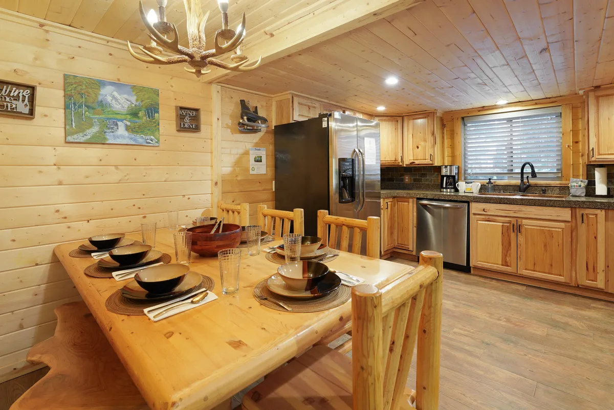A warm, communal dining area showcases a wooden dining table under a chandelier, with kitchen appliances and wall art visible in the background. The setting feels inviting, ideal for shared meals and planning group excursions.
