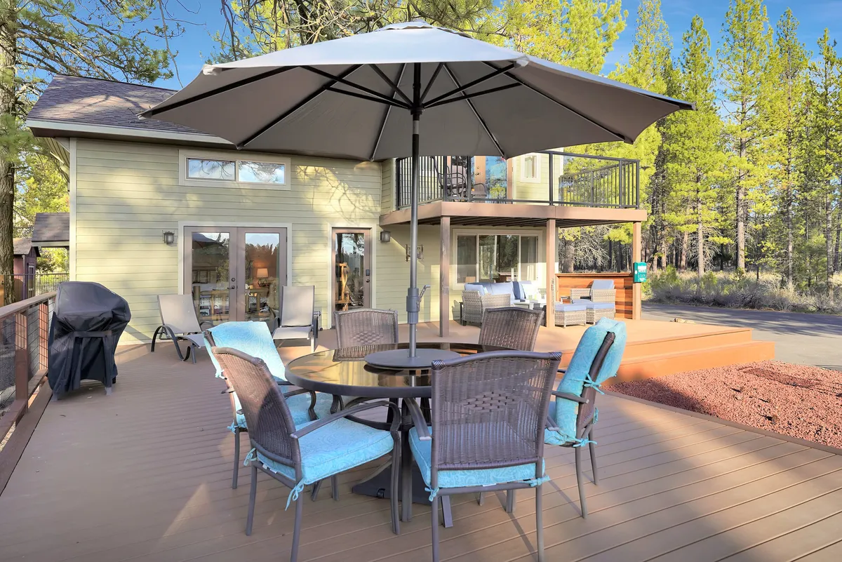 An inviting outdoor dining area with a table, large umbrella, grill, and surrounding trees, creating a relaxed setting for outdoor meals and evening stargazing.