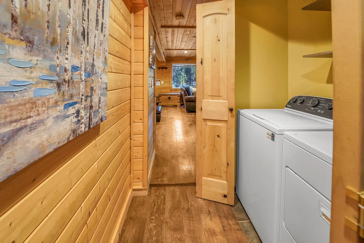 This image features a cozy laundry area with a washing machine set against warm wood paneling, complemented by artwork on the wall and a doorway leading into another room. Natural light filters in, creating a welcoming atmosphere that makes daily chores feel pleasant and convenient.