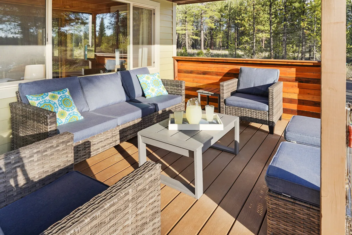 A charming outdoor seating arrangement on a patio, featuring decorative cushions and a coffee table set for refreshments, surrounded by trees and nature. The area feels accessible, relaxed, and perfect for both social gatherings and quiet moments with a pet.
