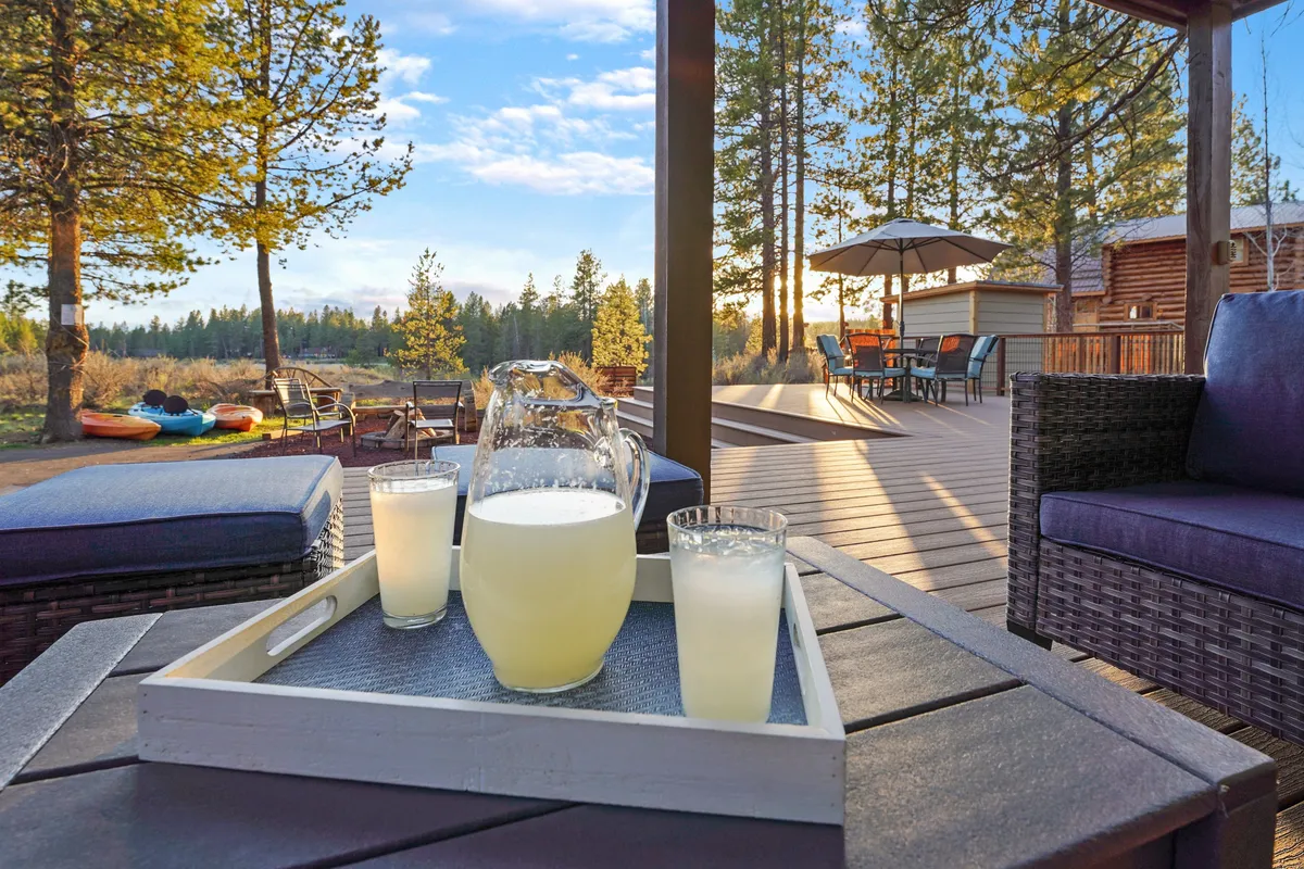 A cheerful outdoor seating area with a deck dining table, a pitcher and glasses of lemonade, and trees in the background. The scene is set for socializing, with ample space for group gatherings, shared drinks, and laughter under the open sky.